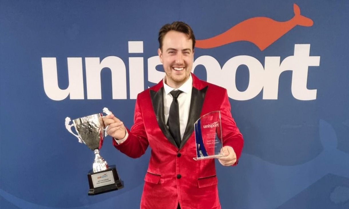 Man in red suit holding two trophies.