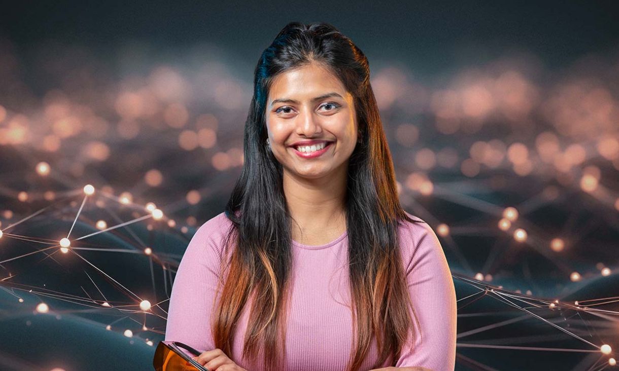 A woman in a pink shirt stands confidently in front of a complex network setup.