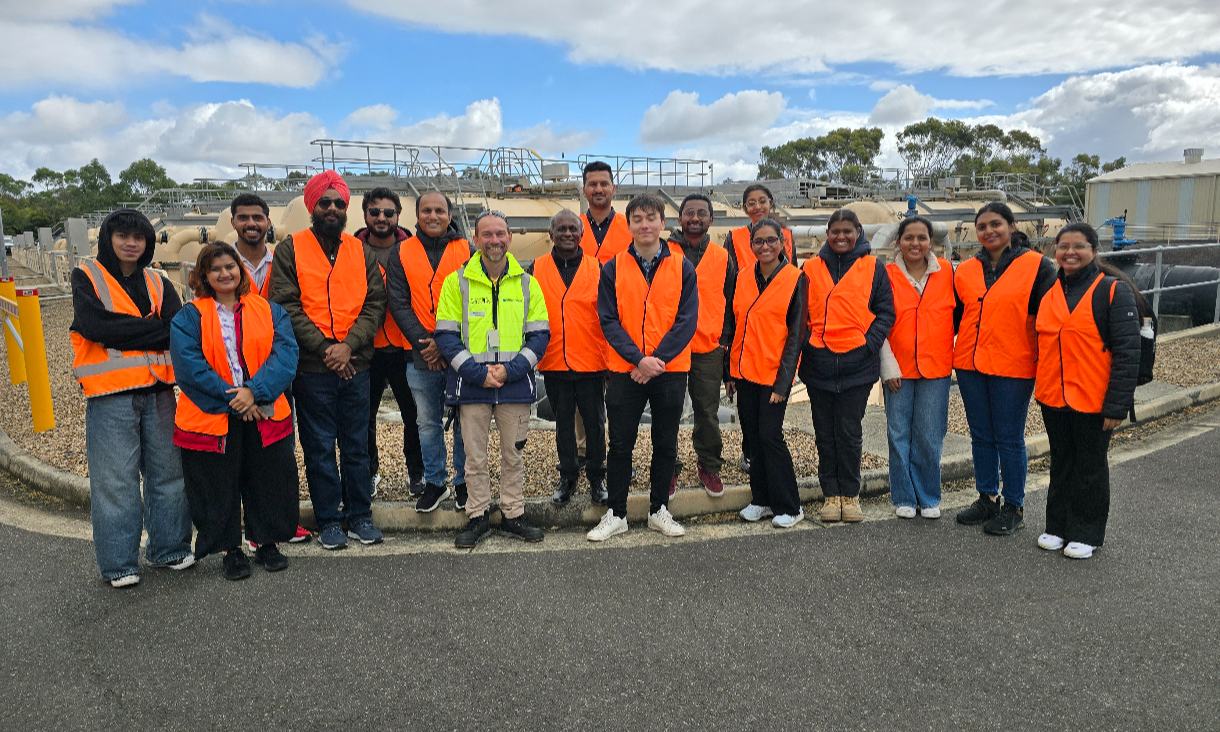 17 people in hi-visibility vests in front of a water treatment plant