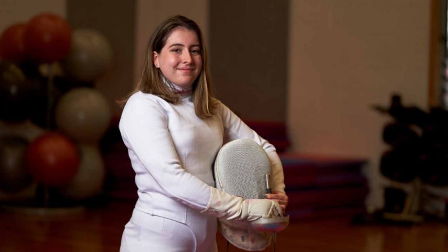 A female fencer smiles at the camera