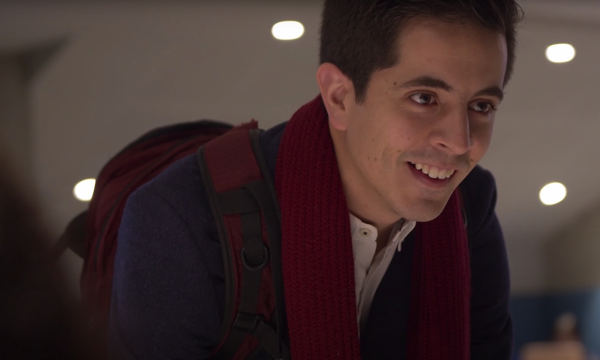 A male student wearing a red scarf smiles at someone not shown in the photo.