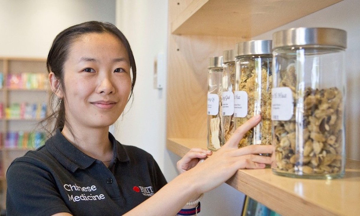 A Chinese Medicine students stands with Chinese herbs.