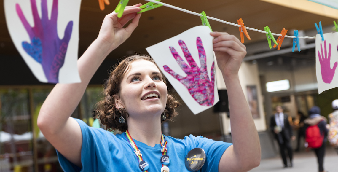 A student smiles as she hangs a painting of a hand on a peg line