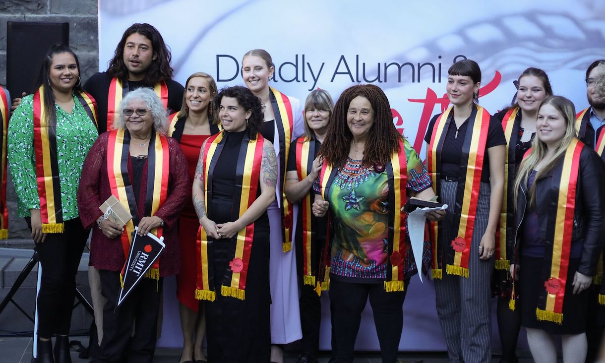 Indigenous Alumni pose for a group photo wearing red, gold and black sashes