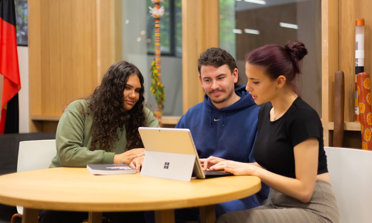 Three people sitting at table with laptop