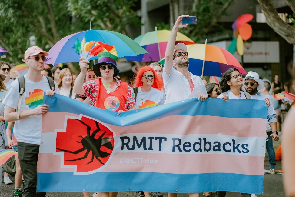 Students march holding a RMIT Redbacks pride-branded banner.