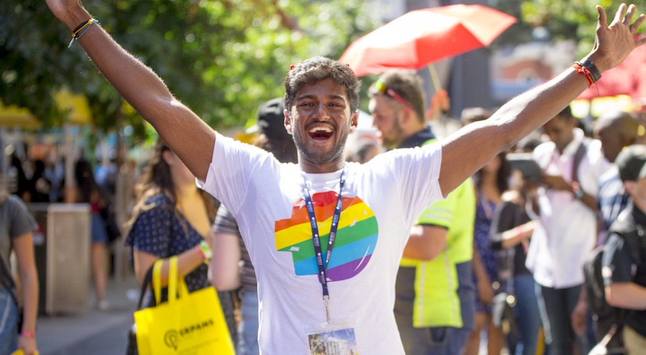 A student waves his arms wearing a shirt with a rainbow RMIT logo.