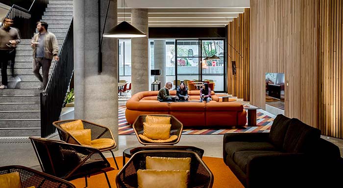 A modern lobby with couches is featured. The words 'Scholarships available' are printed on the photo.