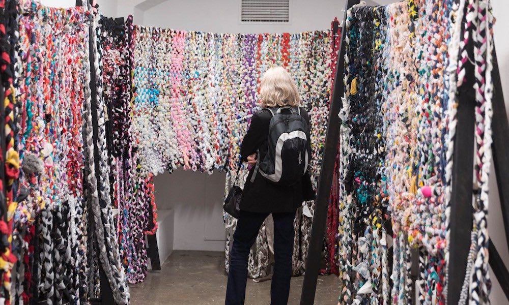 A student examines artwork made from colourful wool and yarn at an exhibition.