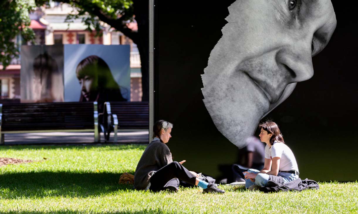 Two people sitting on grass in front of large photo