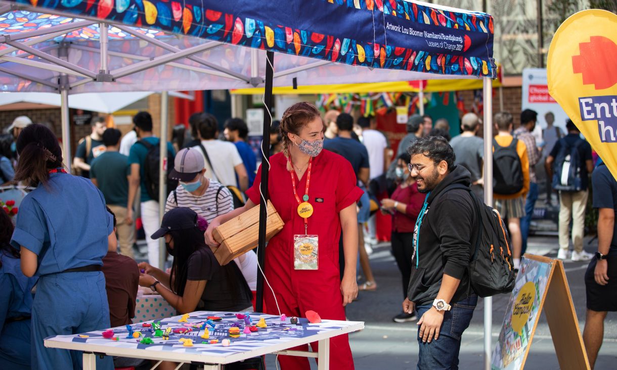 Two students standing at a colourful stall smiling and talking while looking at artwork
