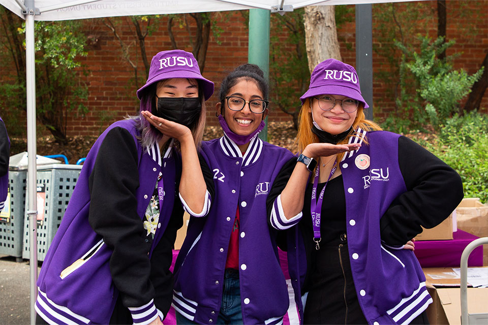 Three women smiling for camera in purple RUSU jackets