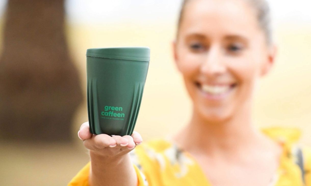 Person holding Green Caffeen cup to camera