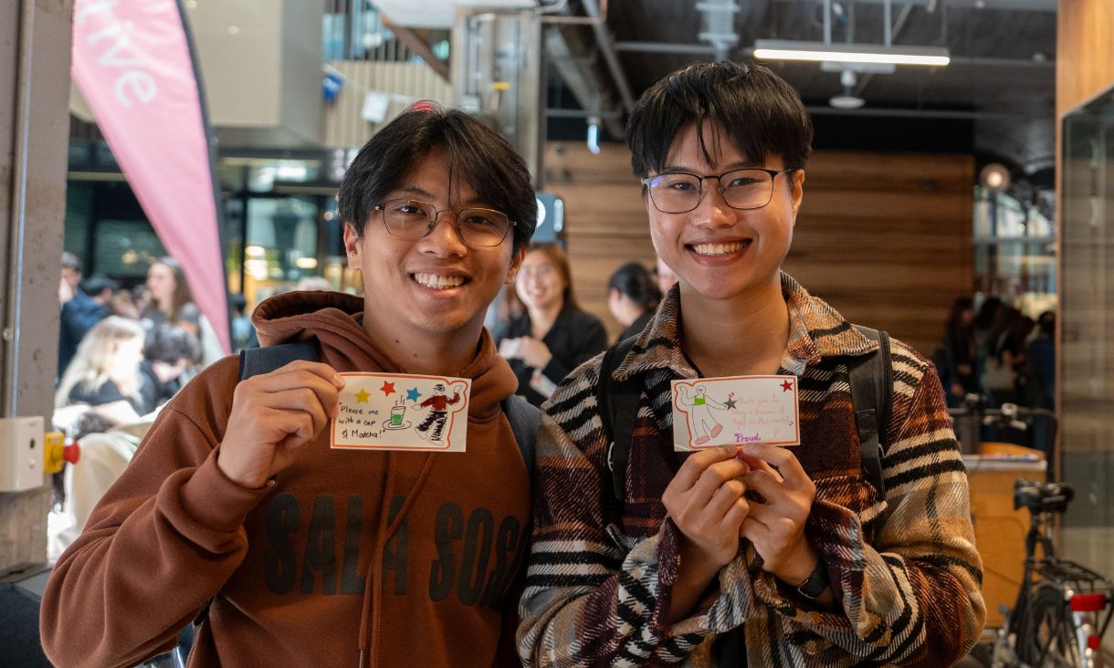two people smiling at camera with paper drawings in hand