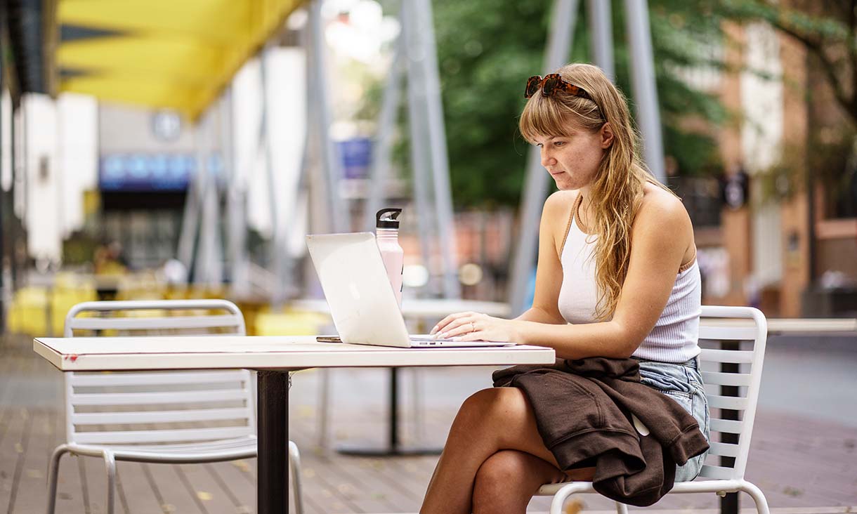 A student sitting at a table outside working on a laptop