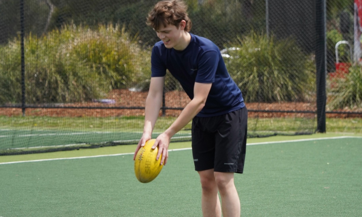 Man about to kick a yellow Australian Football League football 