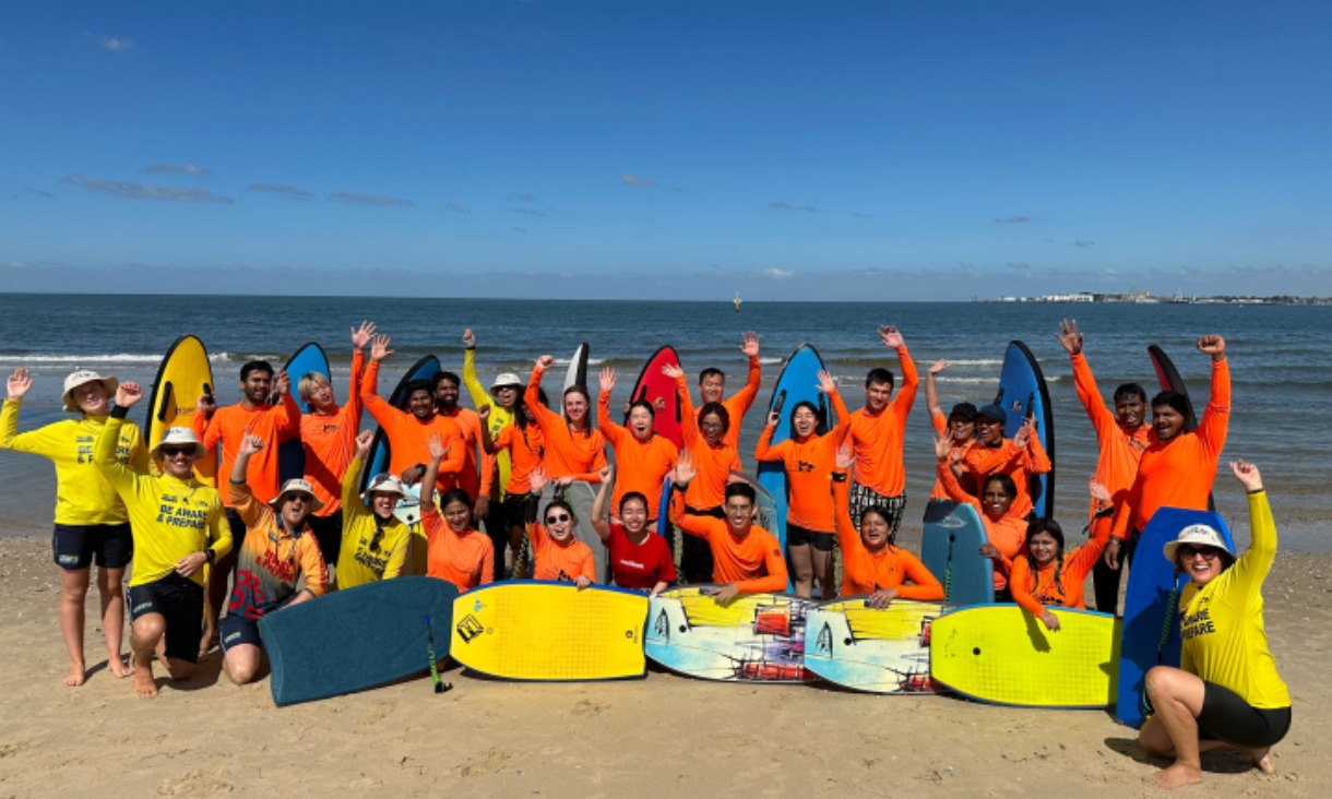 RMIT students hold boogie boards at Port Melbourne Beach during Beach Water Safety Day 2025