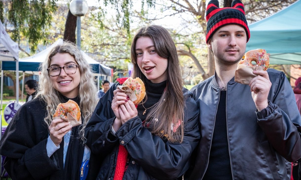 Three students hold donuts and pose for the camera