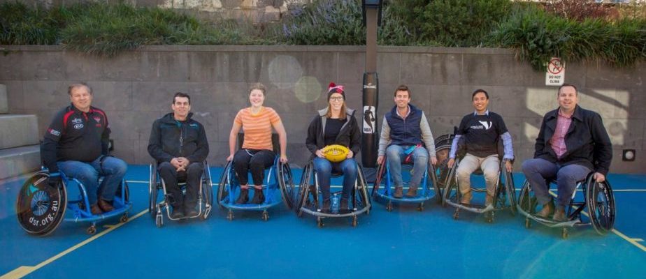 Students pose for a photo in wheelchairs on a basketball court.