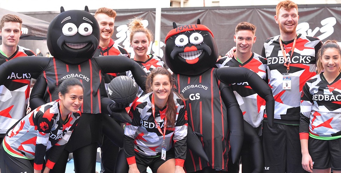 Redbacks mascots (spiders) with RMIT student athletes on a soccer field.