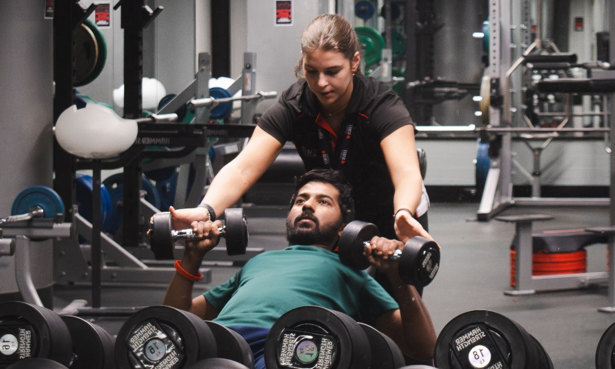 Personal trainer, Antonia Manoglouc supports client lifting weights at RMIT's Active Hub