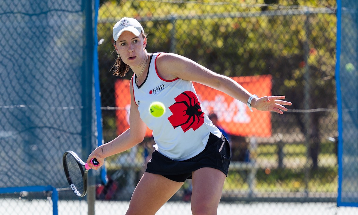 Tennis player in RMIT uniform hits the ball.