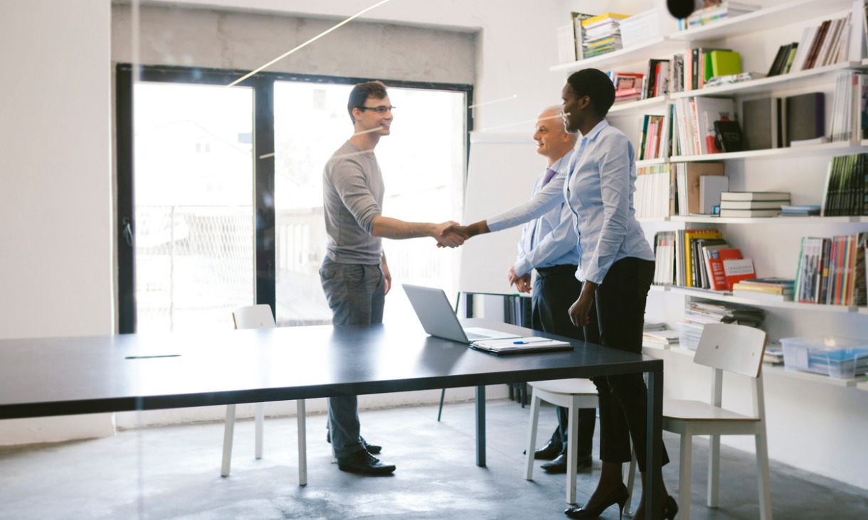 A man shakes a woman's hand while her colleague stands next to her.