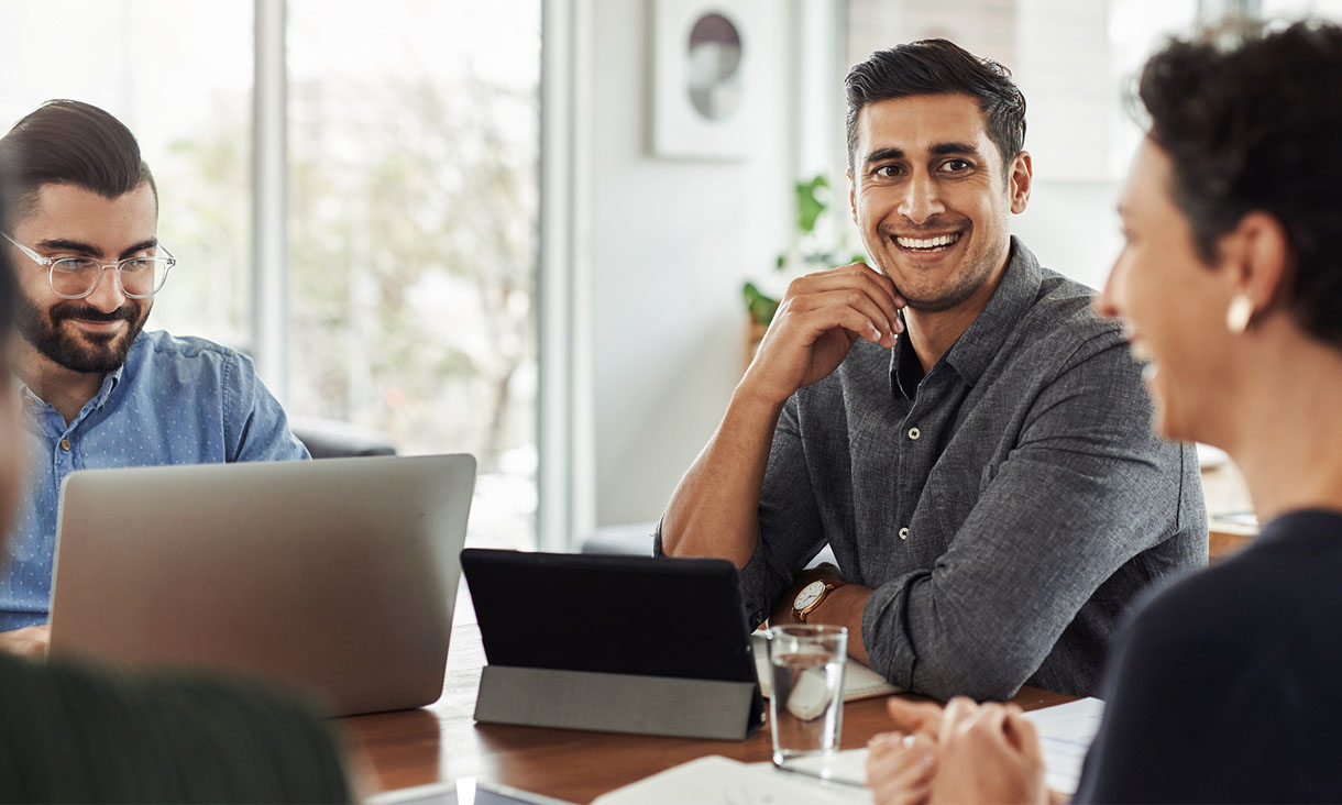 A group of colleagues sit at a round table during a meeting.