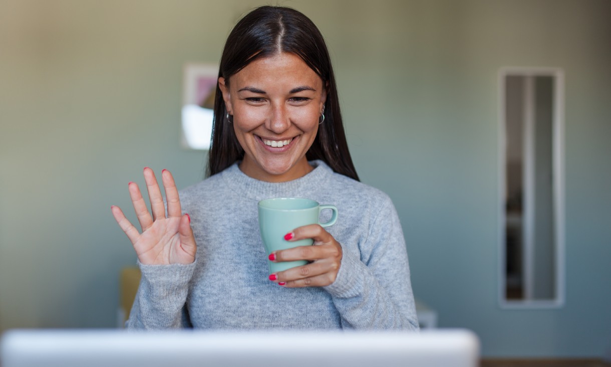 Young woman waving to laptop screen for video meeting