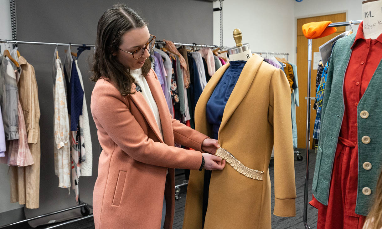 An RMIT fashion student working on an outfit surrounded by costumes on racks