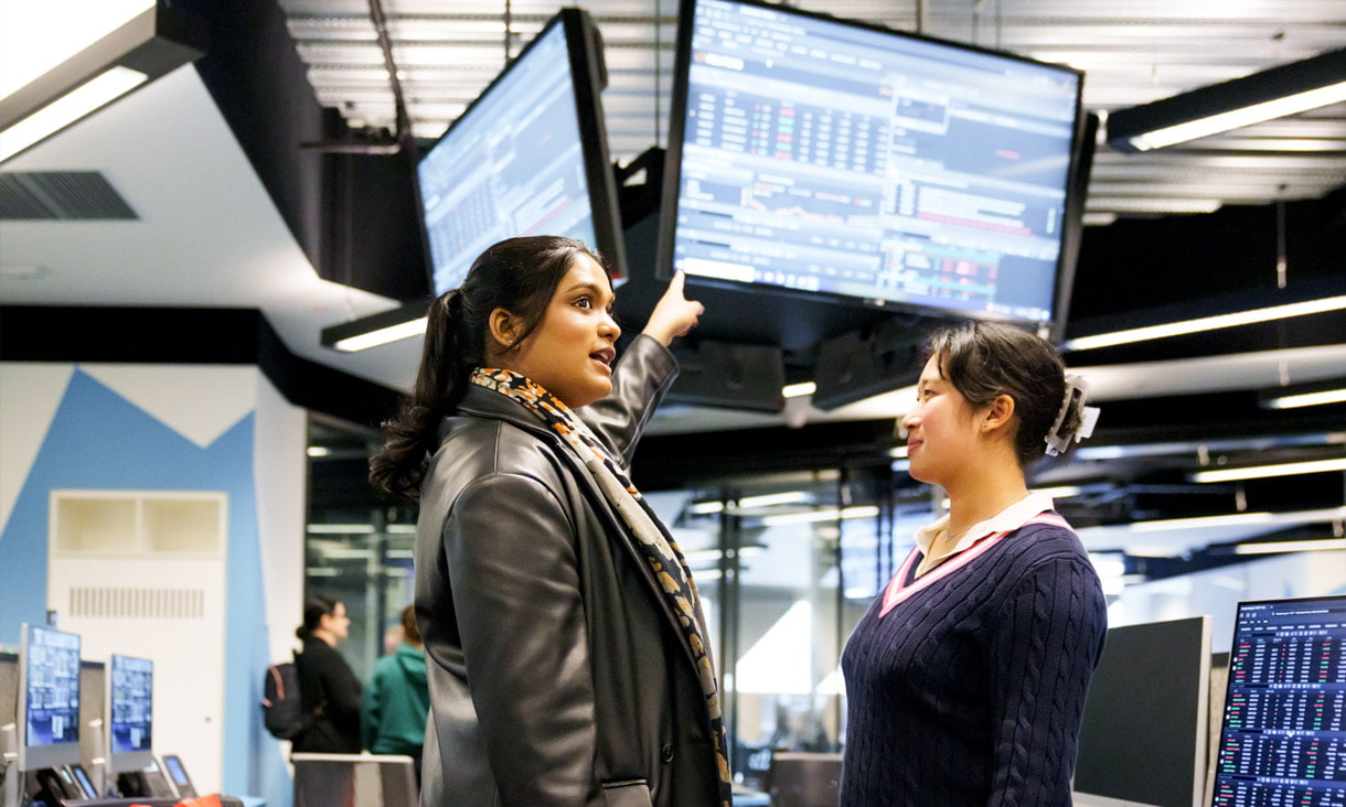 Two business students in RMIT facilities pointing at a screen showing stock trades