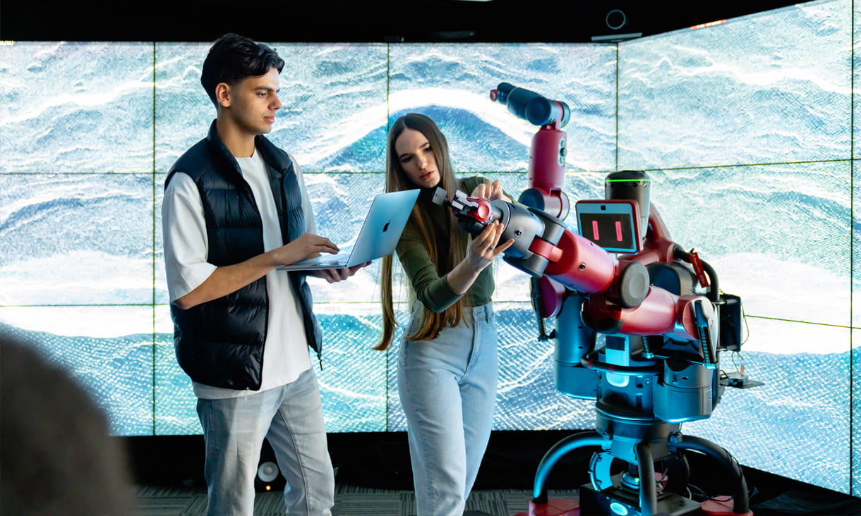 Two RMIT students working on a robot surrounded by display screens