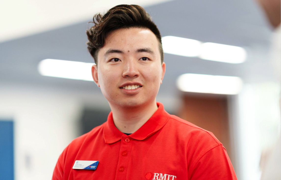 Student in a red RMIT polo shirt and name badge standing indoors, with a blurred background.