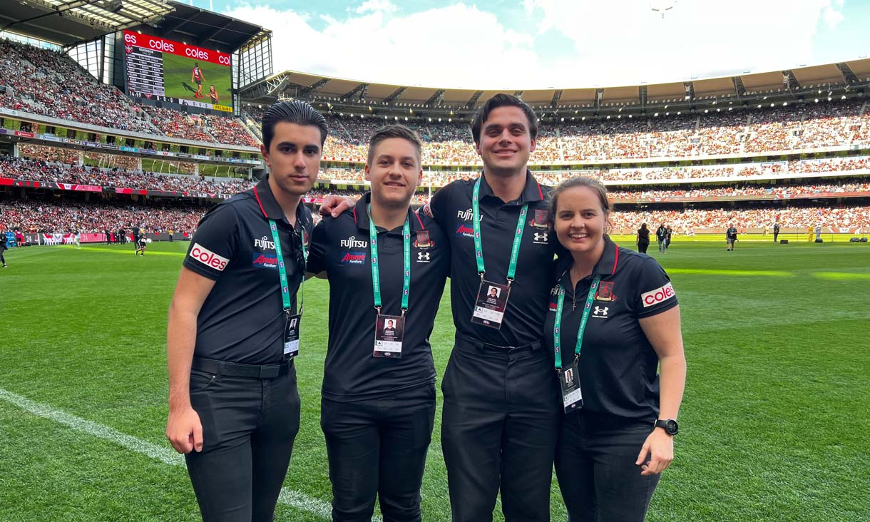 Four RMIT students standing on the boundary line at the MCG, for Essendon Football Club