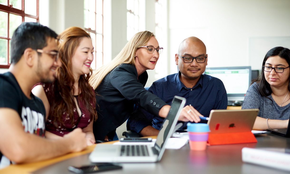 Postgraduate students looking at laptop as tutor points towards screen