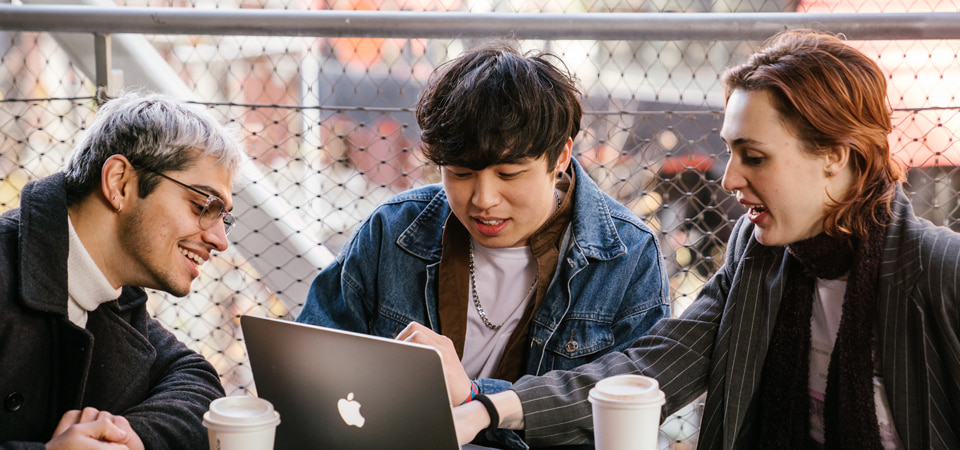 three students sitting around a laptop chatting