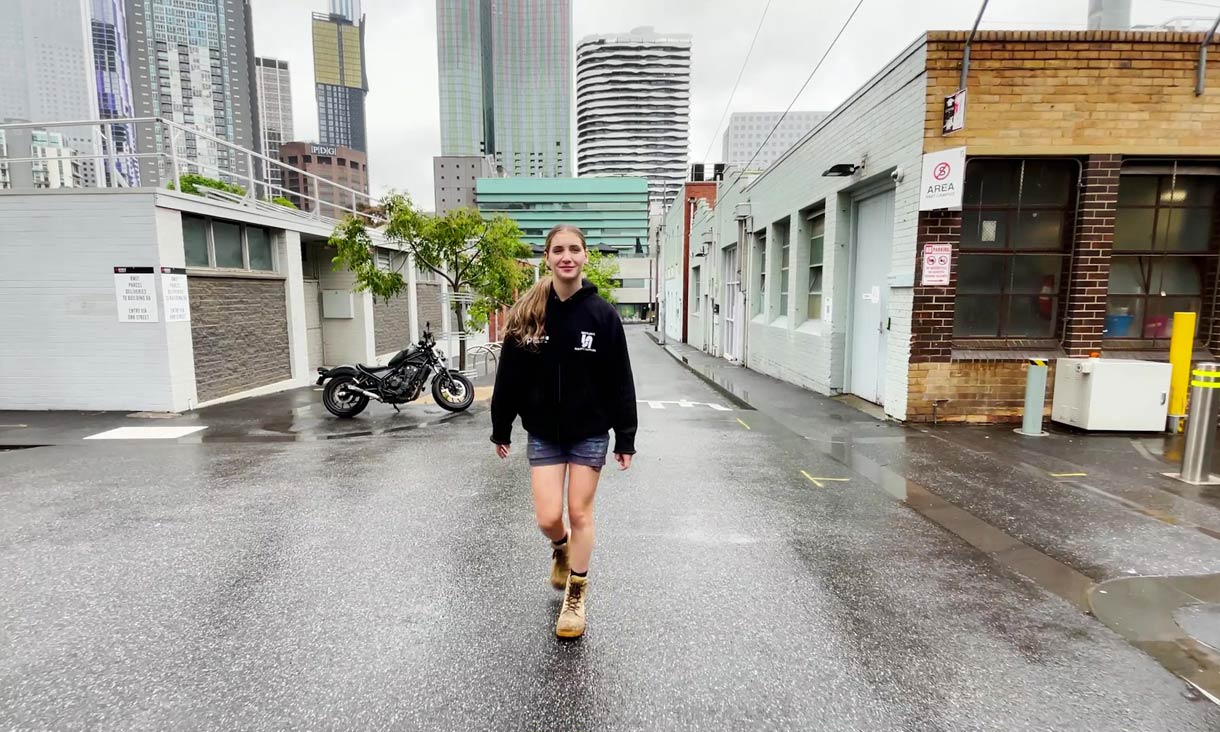 A female trades student walking and talking, towards camera, outside on a rainy Melbourne day