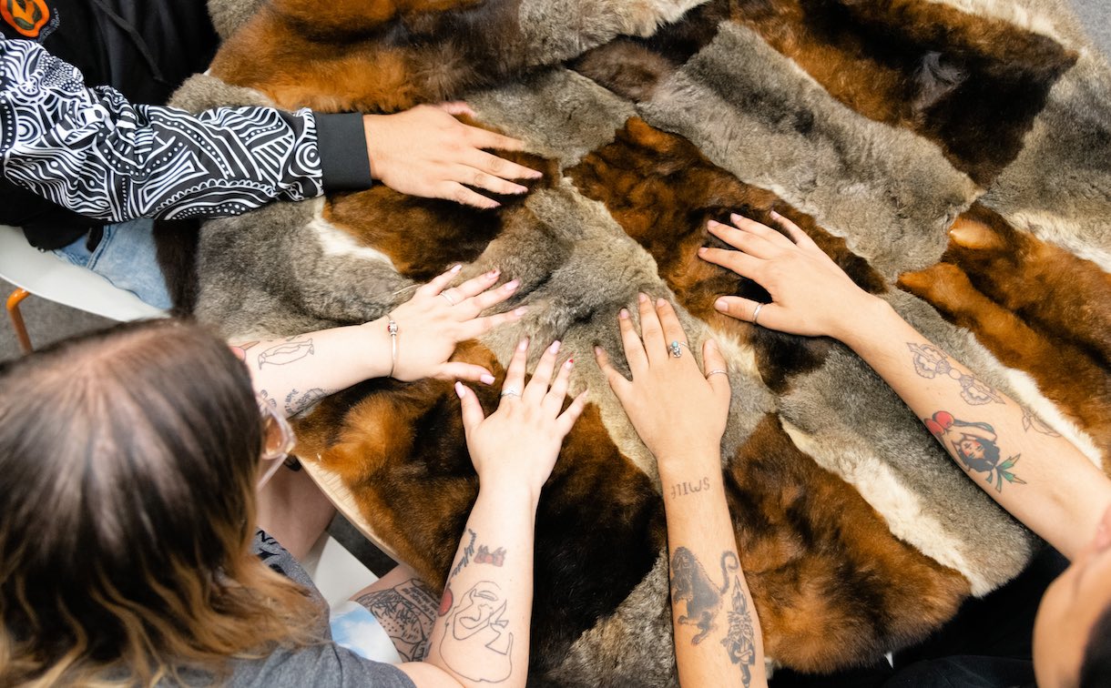 a group of students touching ceremonial furs, the focus is on their hands