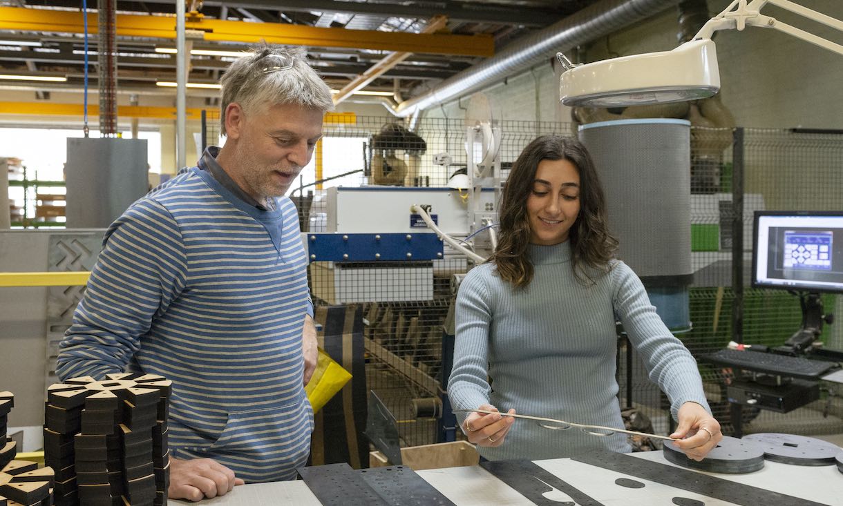 a man and woman looking at a laser cut metal template in a fabrication lab