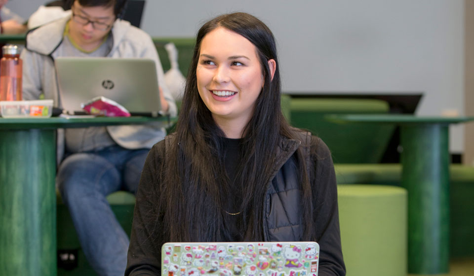 Female student in front of laptop screen, smiling, in a classroom setting