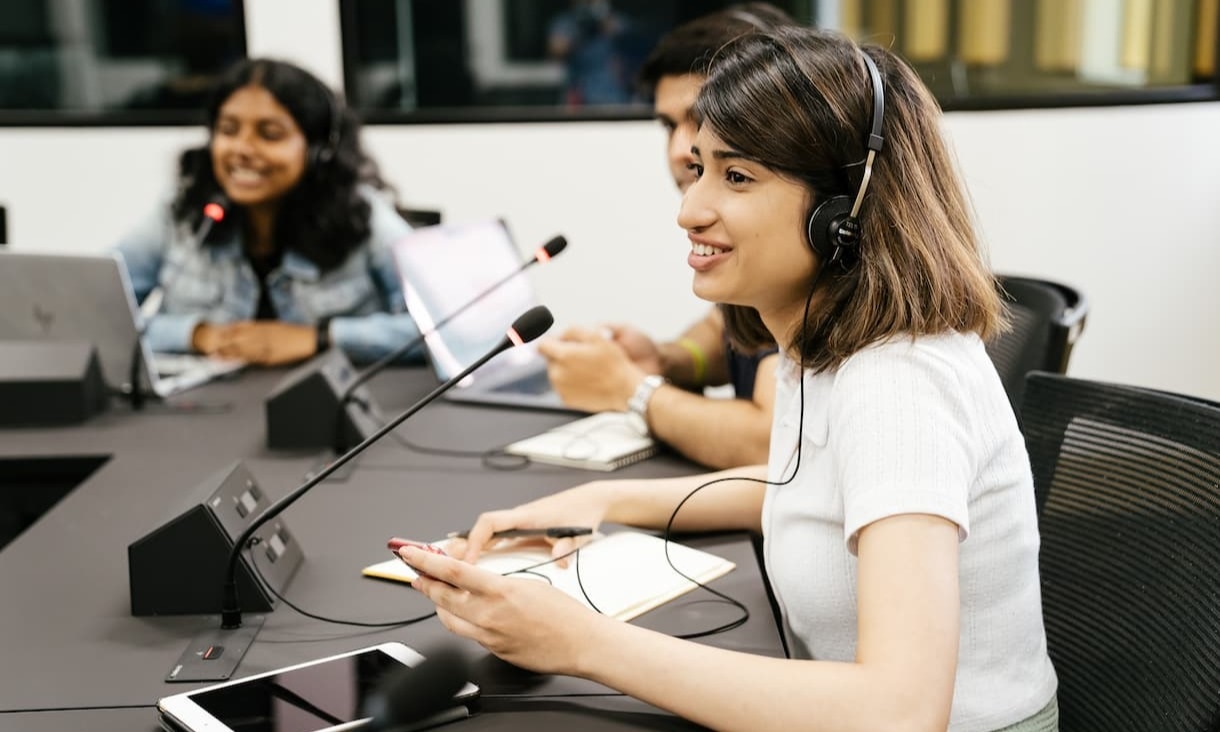 Students wearing headphones at a desk, in front of individual microphones