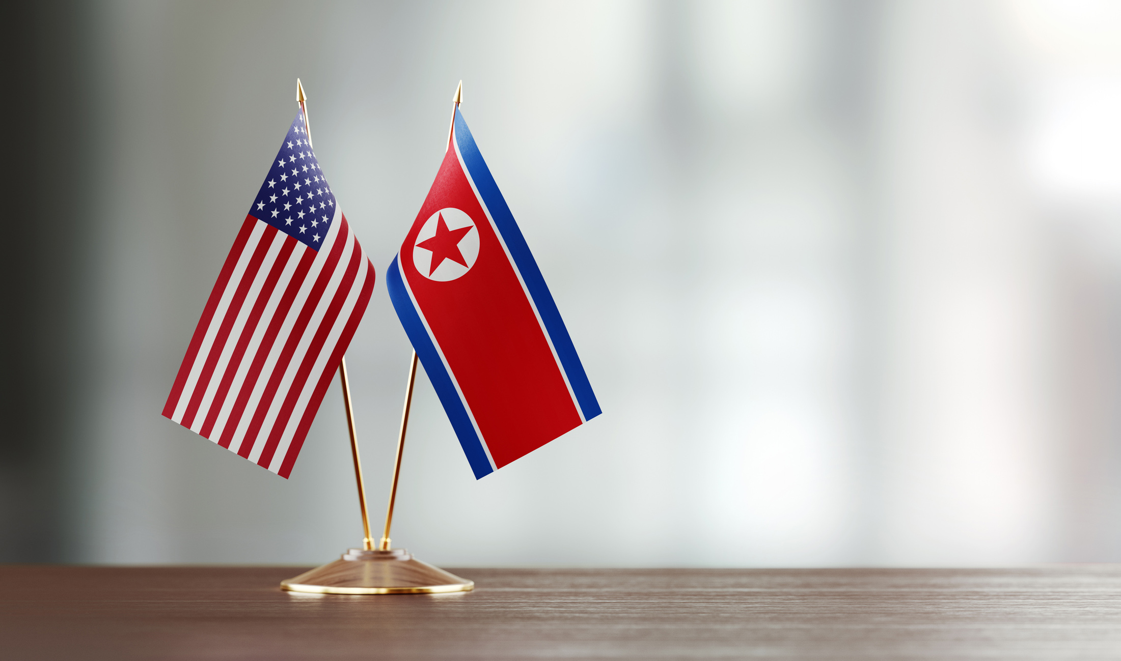 American and North Korean flag pair on desk over defocused background. Horizontal composition with copy space and selective focus.
