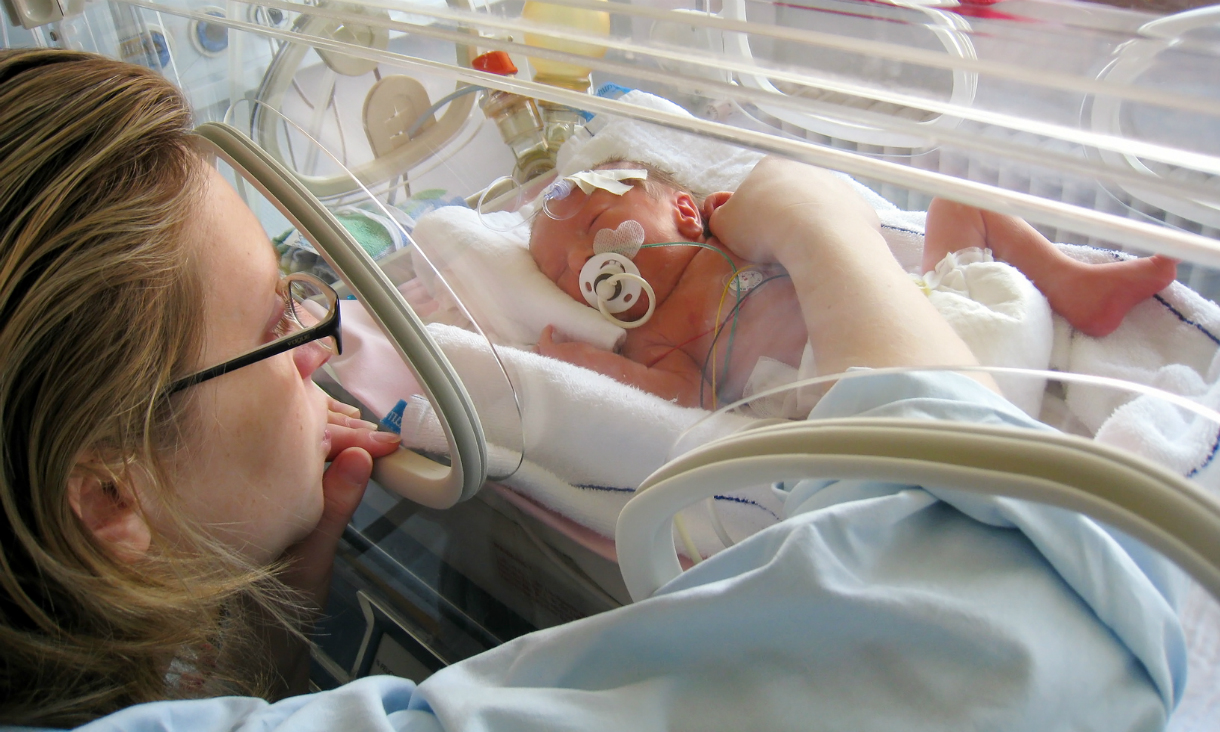 Mother touching her premature baby, who is lying in an incubator