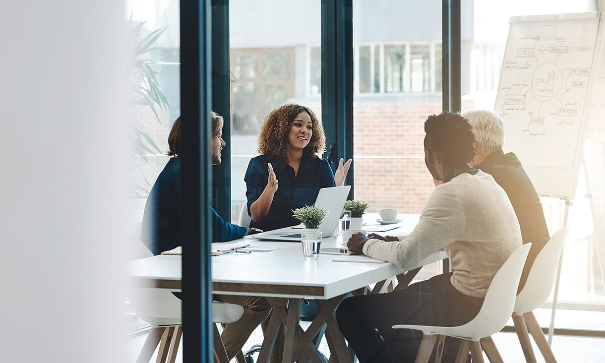 Four people sitting at a desk, having a meeting.