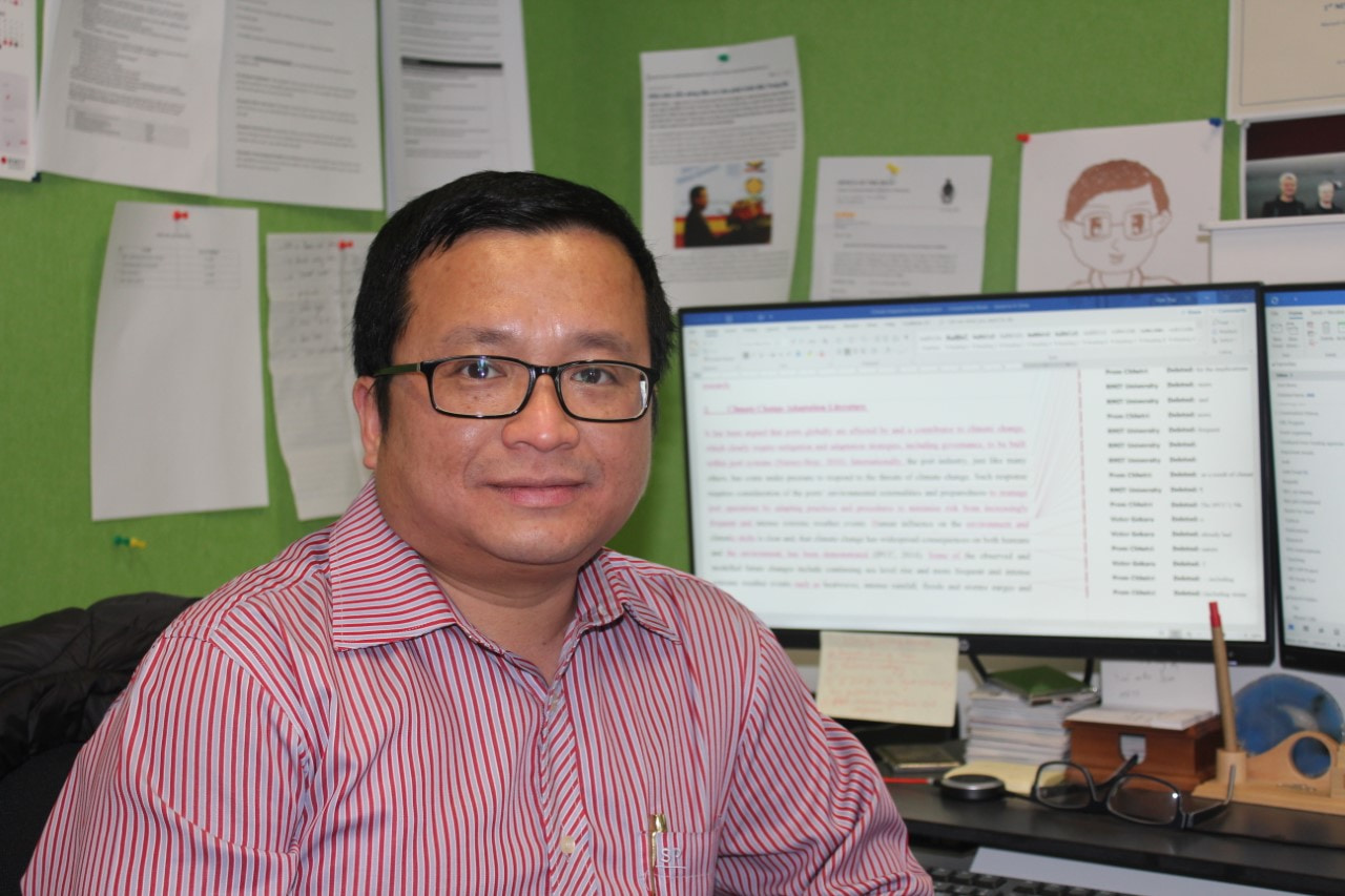 Associate Professor Vinh Thai sits at a desk with a compute in the background.