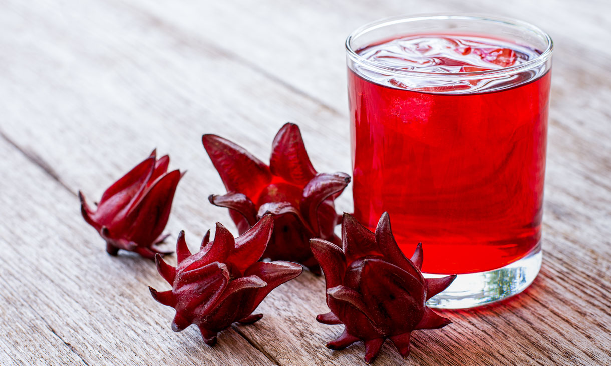A glass of hibiscus tea with hibiscus flowers next to it.