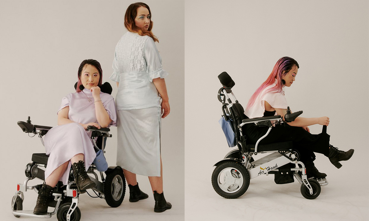 Two people model Rachel Shuggs designs. One model sits on a wheelchair in a purple dress, one stands in a white outfit and another sits in a wheelchair with a purple top and black skirt.