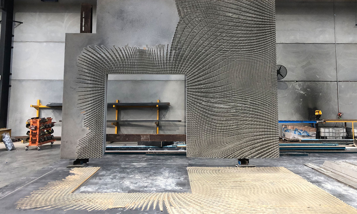 A pre-cast concrete wall with 3D patterns stands above a plywood mold 