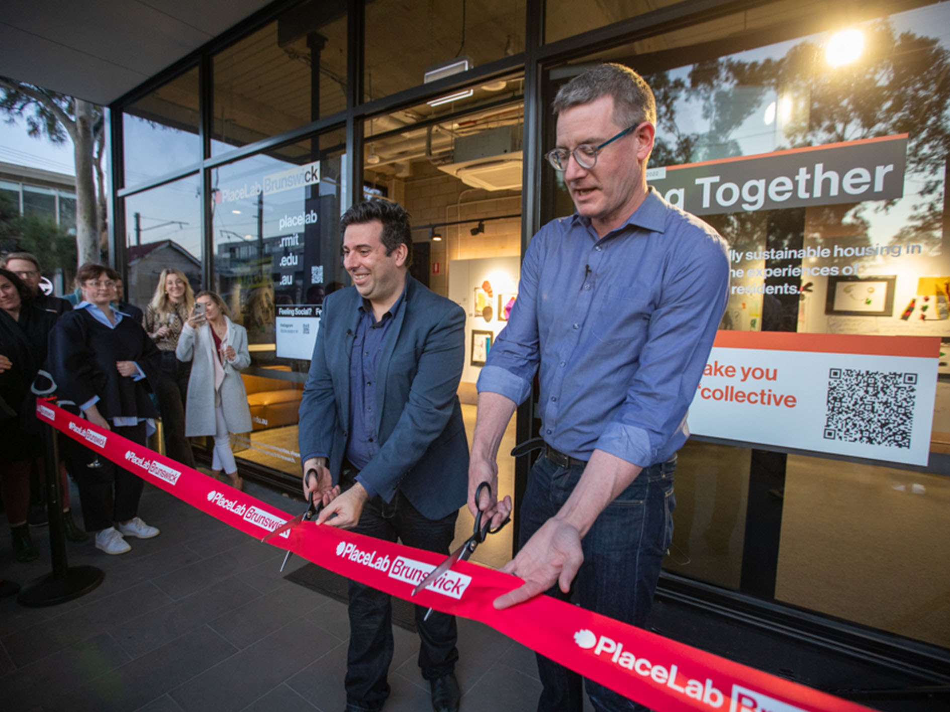 Two people cut a ribbon outside the entrance of PlaceLab Brunswick