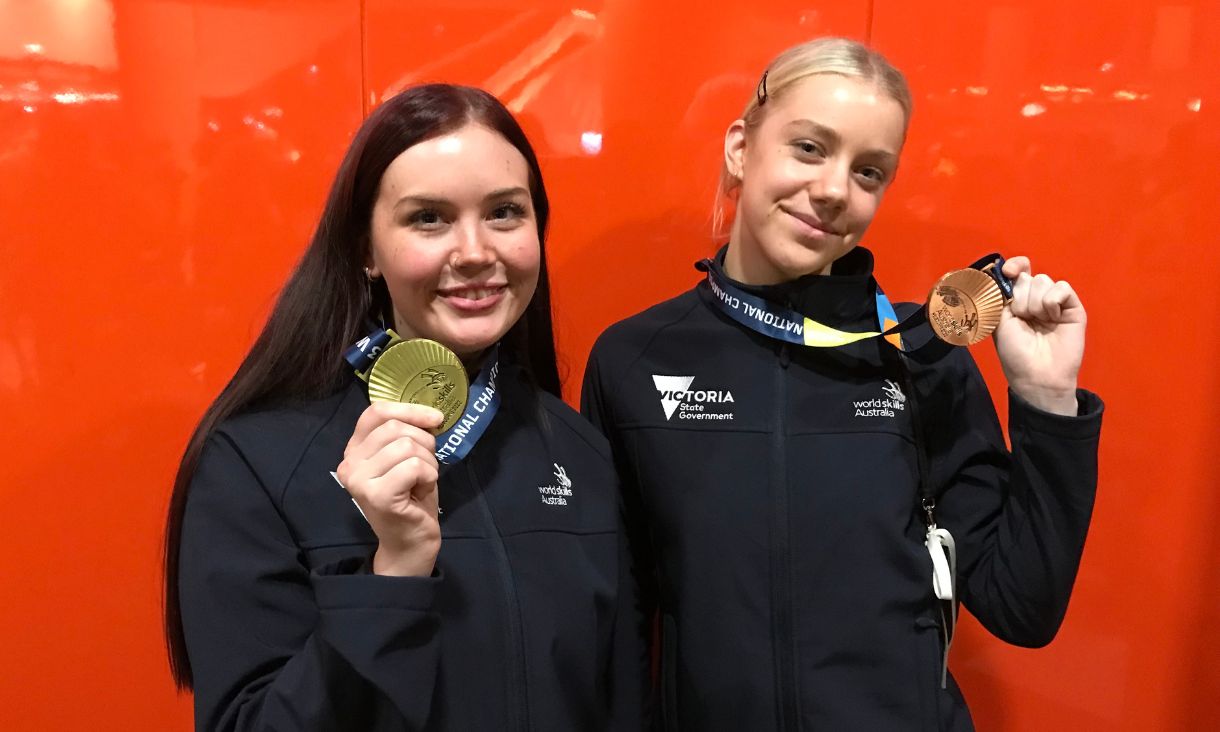 Georgia Knight and Coco Symons smiling and holding gold and bronze medals to camera